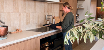 A woman bakes in a kitchen, leaving the oven door open to let heat out