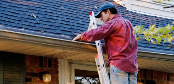 man cleaning leaves out of the roof gutters