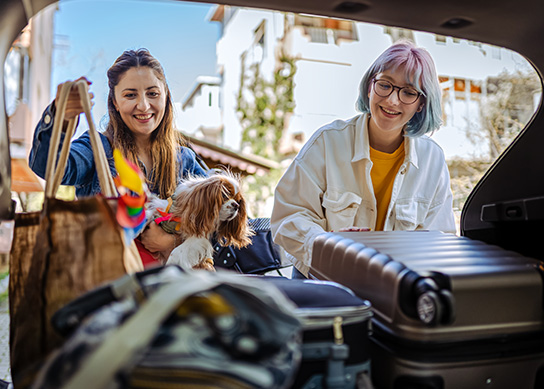 Two happy holidaymakers taking their luggage out of the car.