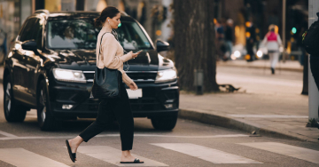 A woman looking at her mobile phone crossing the road.
