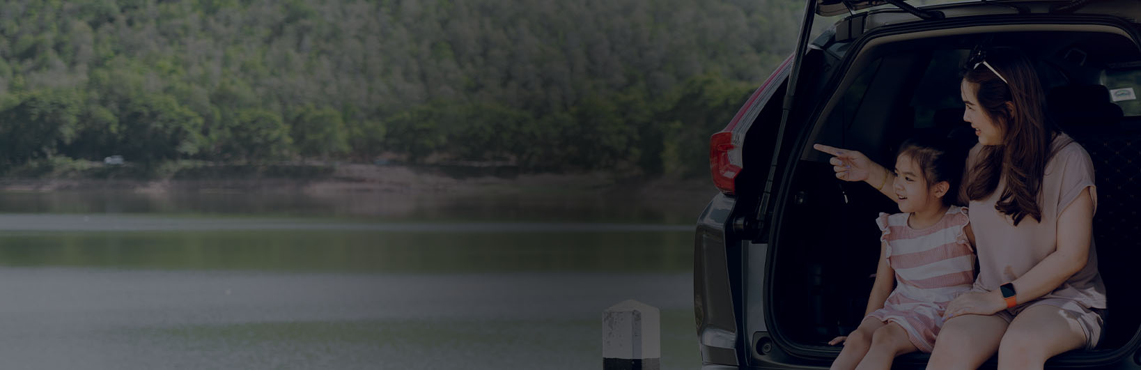 A mum and child admiring a lakeside view from their car.