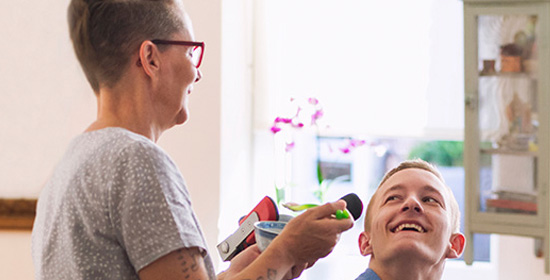 a female carer feeds a smiling man