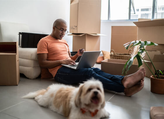 A man surrounded by cardboard boxes viewing his laptop screen in his new home.